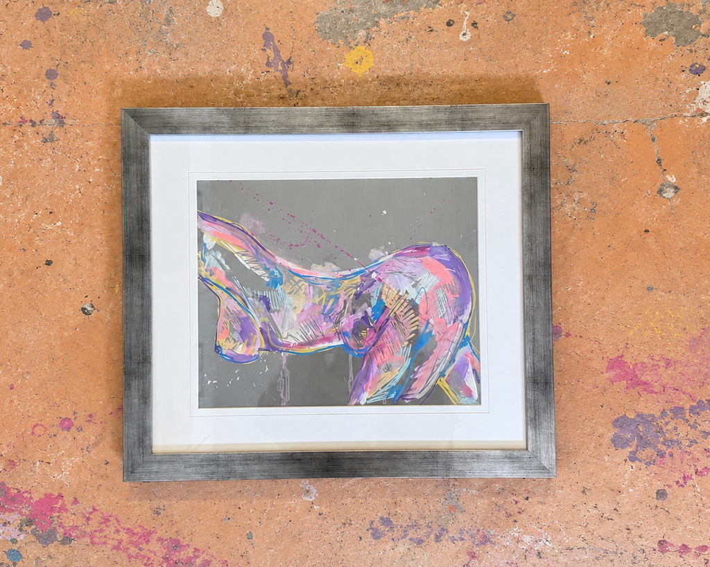 A framed abstract art painting featuring a colorful, textured depiction of a female torso in shades of pink, purple, and blue on a gray background, set in a rustic gray wood frame with a white mat, displayed on a textured orange wall with paint splatters.
